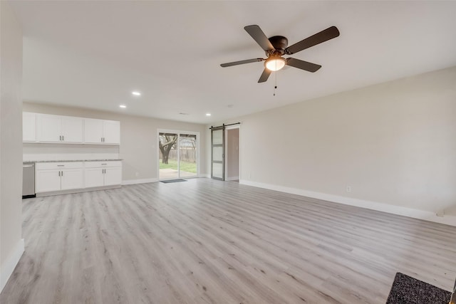 unfurnished living room with a barn door, ceiling fan, and light hardwood / wood-style flooring