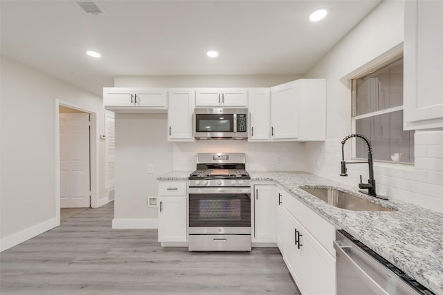 kitchen with sink, stainless steel appliances, white cabinets, and light stone countertops