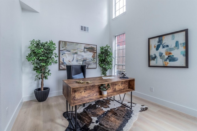 home office with a towering ceiling and light hardwood / wood-style flooring