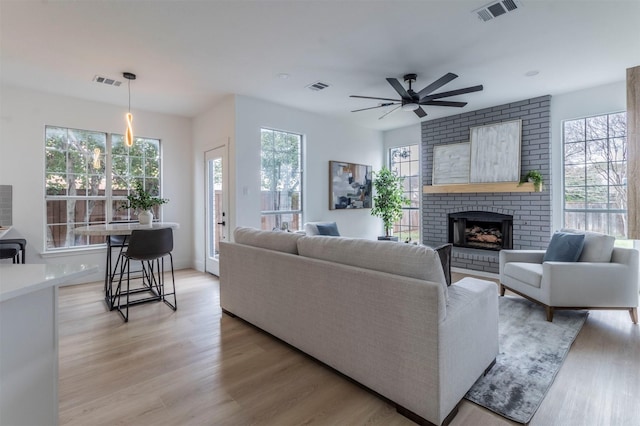 living room featuring a brick fireplace, plenty of natural light, ceiling fan, and light hardwood / wood-style flooring