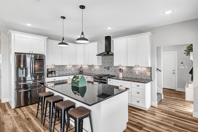 kitchen featuring wall chimney range hood, appliances with stainless steel finishes, white cabinets, and a center island