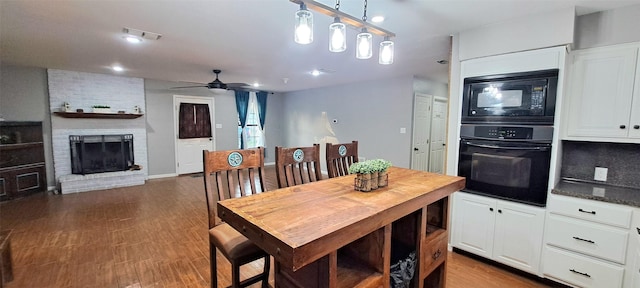 dining space with a brick fireplace, dark wood-type flooring, and ceiling fan