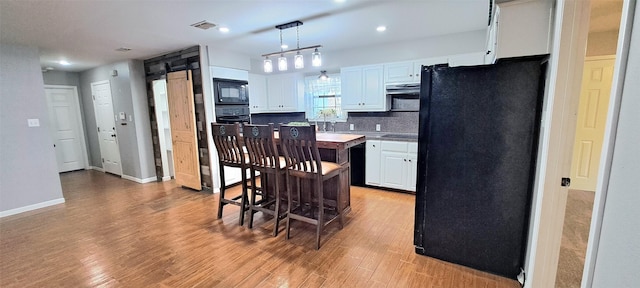 kitchen with tasteful backsplash, black appliances, hanging light fixtures, light hardwood / wood-style floors, and white cabinets