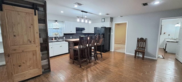 kitchen featuring black refrigerator, white cabinetry, range hood, and hanging light fixtures