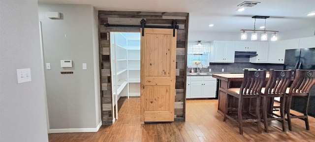 kitchen with sink, black fridge, decorative light fixtures, a barn door, and white cabinets