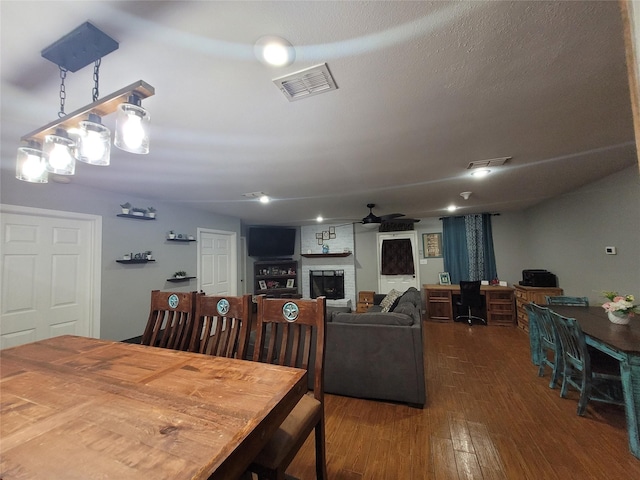 dining room featuring a large fireplace, a textured ceiling, dark hardwood / wood-style floors, and ceiling fan