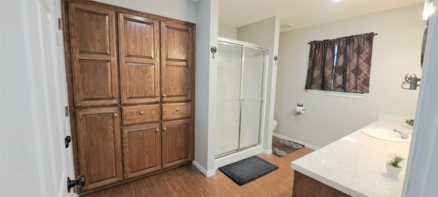 bathroom featuring wood-type flooring, toilet, a shower with door, and vanity