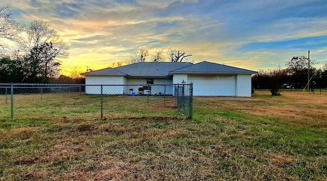 back house at dusk featuring a garage and a lawn