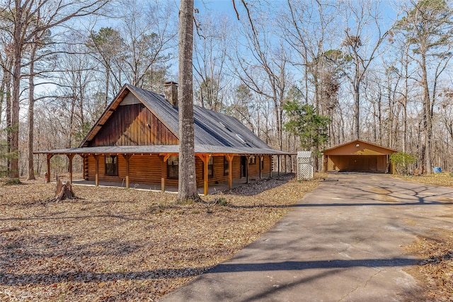 view of side of home featuring log exterior, a chimney, aphalt driveway, covered porch, and a carport