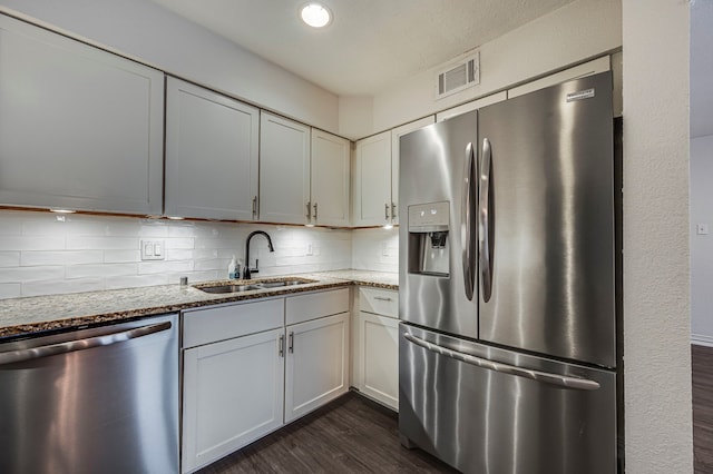 kitchen featuring sink, dark wood-type flooring, stainless steel appliances, tasteful backsplash, and light stone countertops