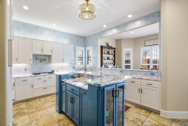 kitchen with blue cabinetry, light stone countertops, stainless steel gas cooktop, white cabinets, and kitchen peninsula