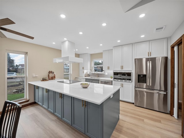 kitchen with light stone counters, island range hood, white cabinets, and appliances with stainless steel finishes