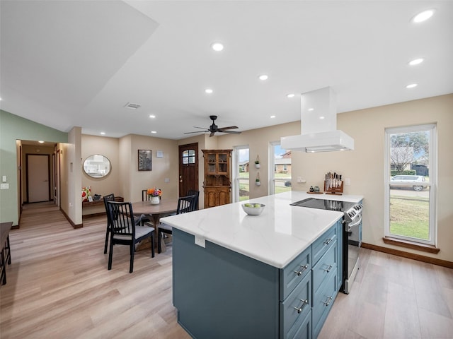 kitchen with blue cabinets, ceiling fan, electric stove, island exhaust hood, and light hardwood / wood-style floors