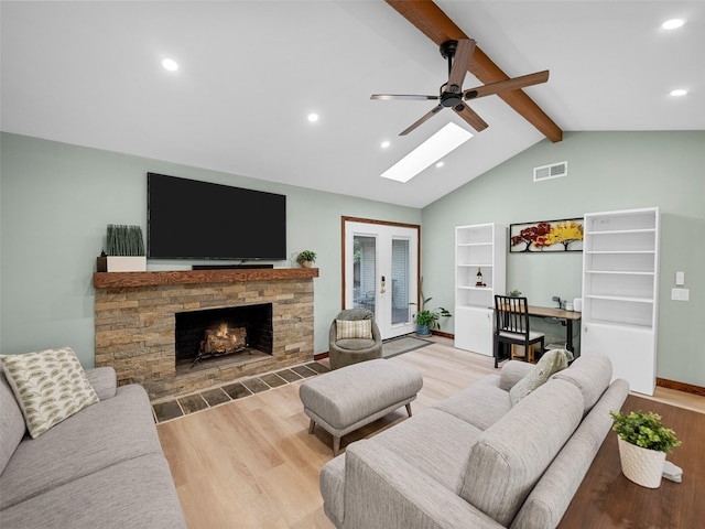 living room with french doors, vaulted ceiling with skylight, ceiling fan, a fireplace, and light hardwood / wood-style floors