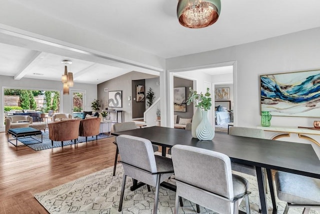 dining room featuring a notable chandelier, light hardwood / wood-style floors, and vaulted ceiling with beams