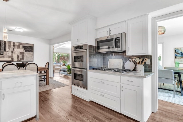 kitchen featuring pendant lighting, white cabinetry, stainless steel appliances, decorative backsplash, and light wood-type flooring