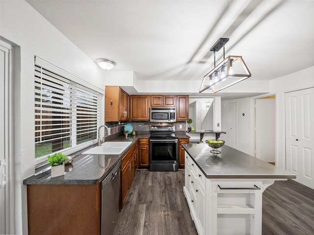 kitchen with brown cabinetry, dark countertops, stainless steel appliances, pendant lighting, and a sink