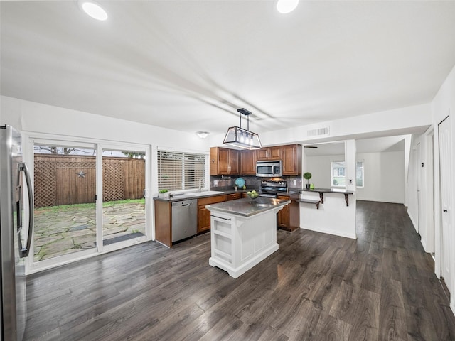 kitchen with pendant lighting, appliances with stainless steel finishes, brown cabinetry, a kitchen island, and a kitchen bar