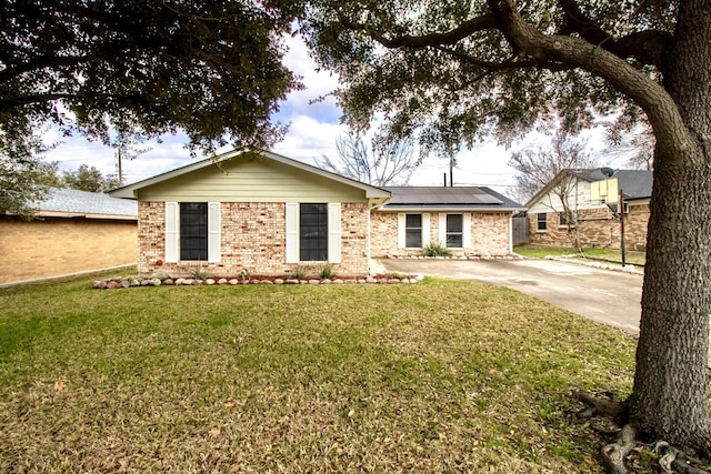 single story home featuring solar panels, brick siding, a front yard, and driveway