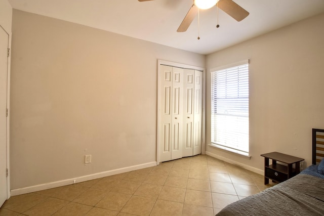 unfurnished bedroom featuring ceiling fan, baseboards, a closet, and light tile patterned flooring