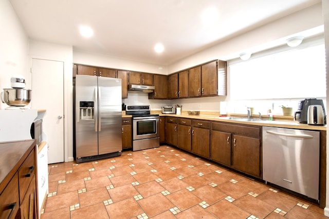 kitchen featuring appliances with stainless steel finishes, light countertops, a sink, and under cabinet range hood