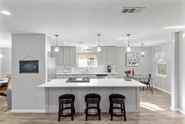 kitchen featuring tasteful backsplash, gray cabinetry, a breakfast bar area, a chandelier, and stainless steel appliances