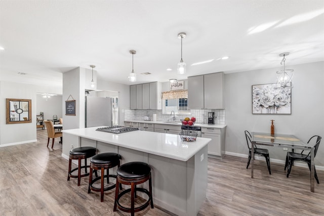 kitchen featuring sink, gray cabinets, stainless steel appliances, a kitchen breakfast bar, and decorative backsplash