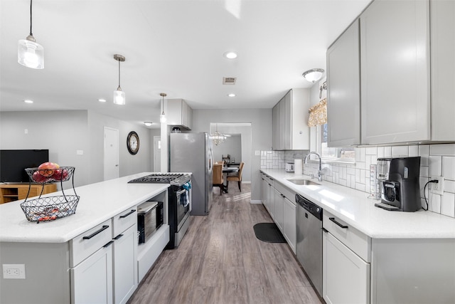 kitchen with sink, hanging light fixtures, appliances with stainless steel finishes, light hardwood / wood-style floors, and backsplash