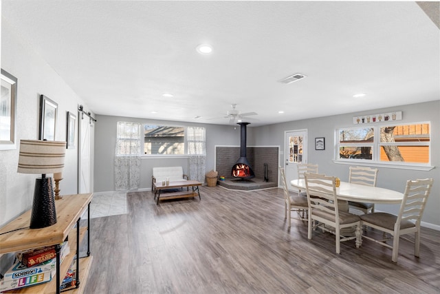 dining space with wood-type flooring, a wood stove, and ceiling fan