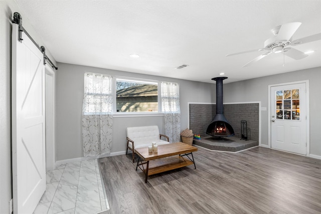 sitting room with light hardwood / wood-style flooring, a barn door, ceiling fan, and a wood stove