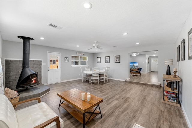 living room with wood-type flooring, ceiling fan, and a wood stove