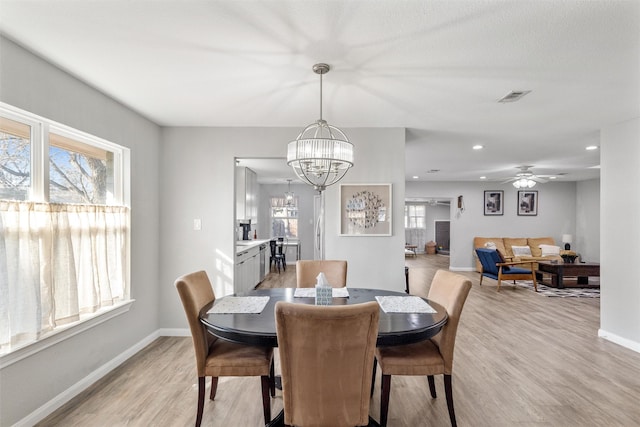 dining room featuring ceiling fan with notable chandelier and light hardwood / wood-style flooring