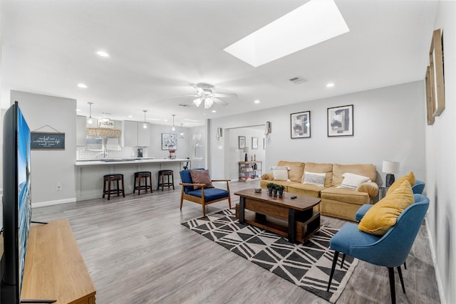 living room featuring ceiling fan, a skylight, and light hardwood / wood-style floors