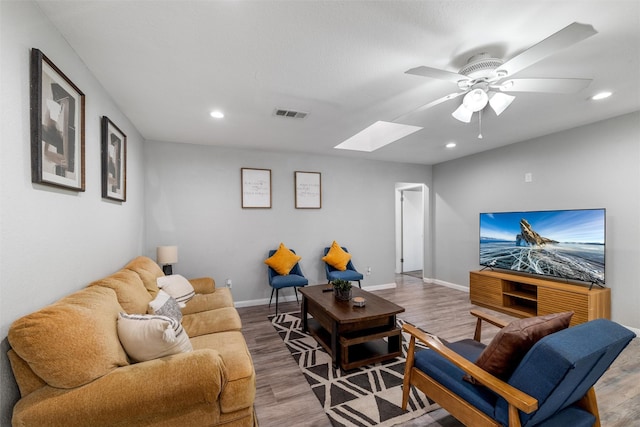 living room featuring hardwood / wood-style flooring, ceiling fan, and a skylight