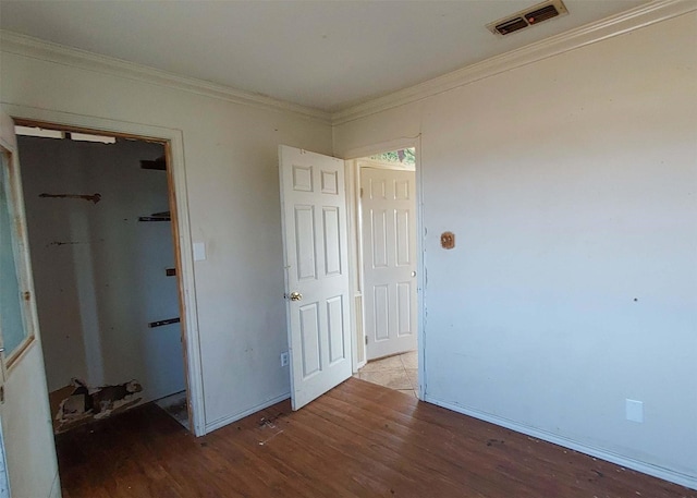 unfurnished bedroom with crown molding, a walk in closet, wood-type flooring, and a closet