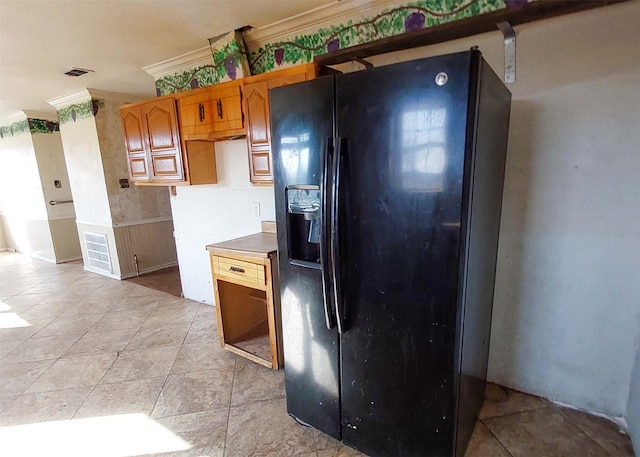 kitchen with black fridge, ornamental molding, and light tile patterned floors