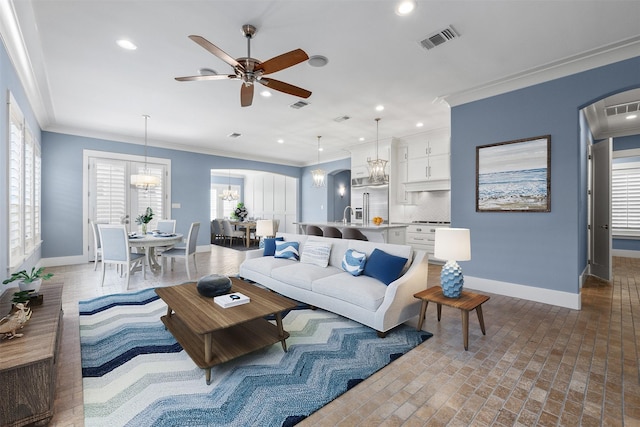 living room featuring crown molding, ceiling fan with notable chandelier, sink, and a wealth of natural light