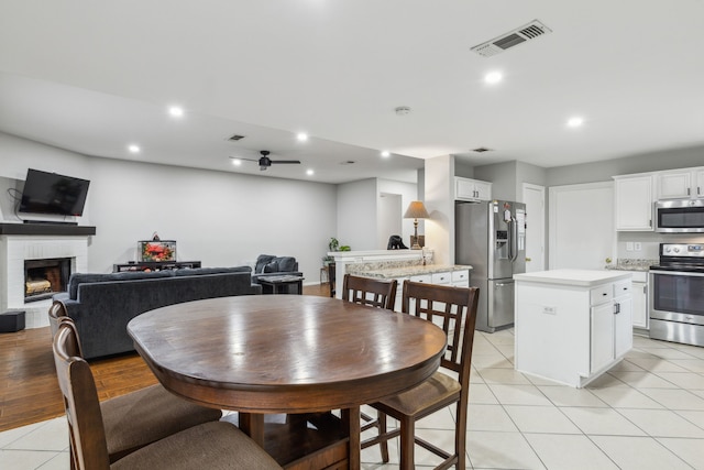 tiled dining area featuring a brick fireplace and ceiling fan