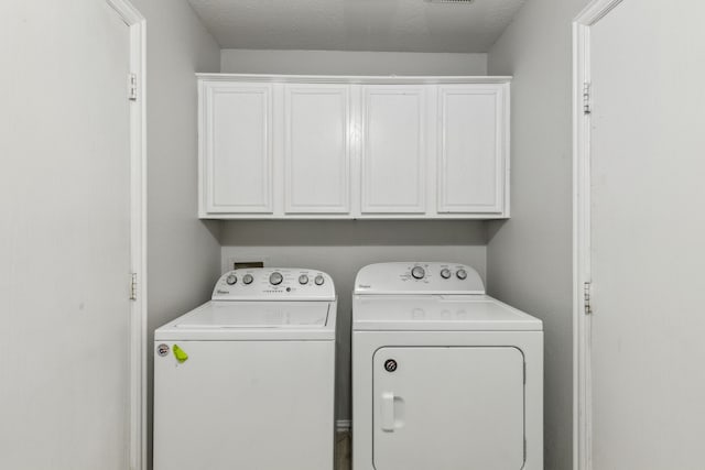 clothes washing area with cabinets, washer and clothes dryer, and a textured ceiling