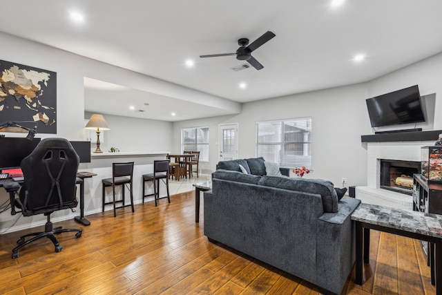 living room with wood-type flooring, ceiling fan, and a fireplace