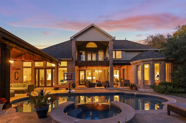 back house at dusk with a balcony, a patio area, a pool with hot tub, ceiling fan, and outdoor lounge area