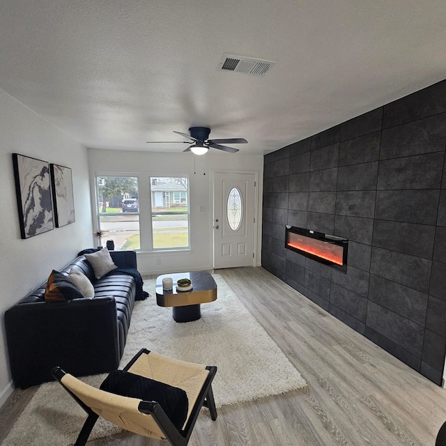 living room with a tiled fireplace, ceiling fan, a textured ceiling, and light hardwood / wood-style floors