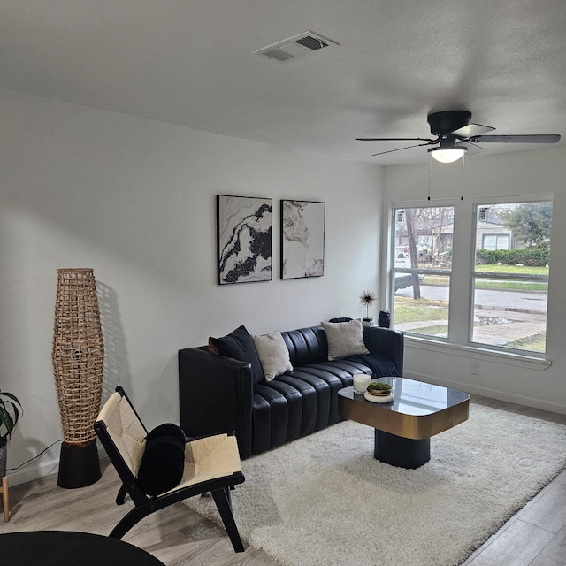 living room with a textured ceiling, ceiling fan, and light wood-type flooring