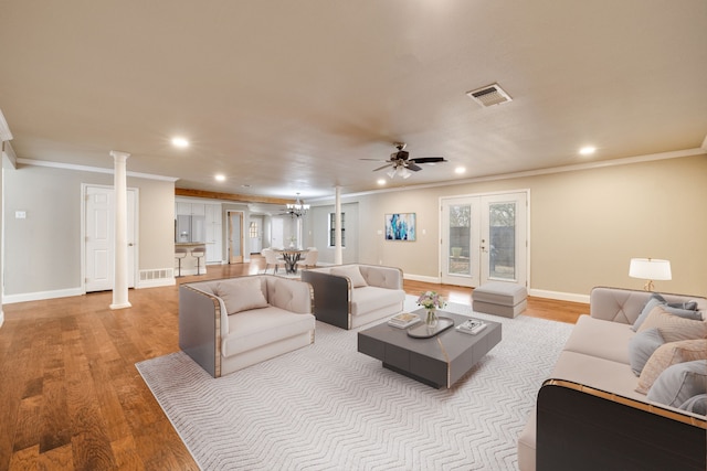 living room with crown molding, light hardwood / wood-style flooring, decorative columns, ceiling fan with notable chandelier, and french doors