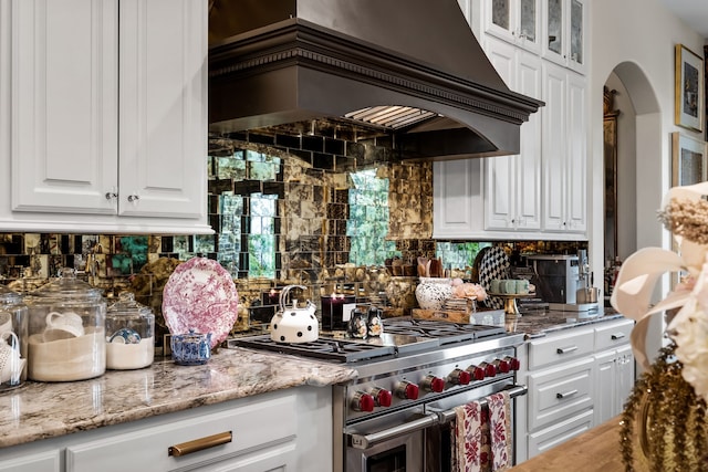 kitchen featuring premium range hood, tasteful backsplash, white cabinets, range with two ovens, and light stone countertops