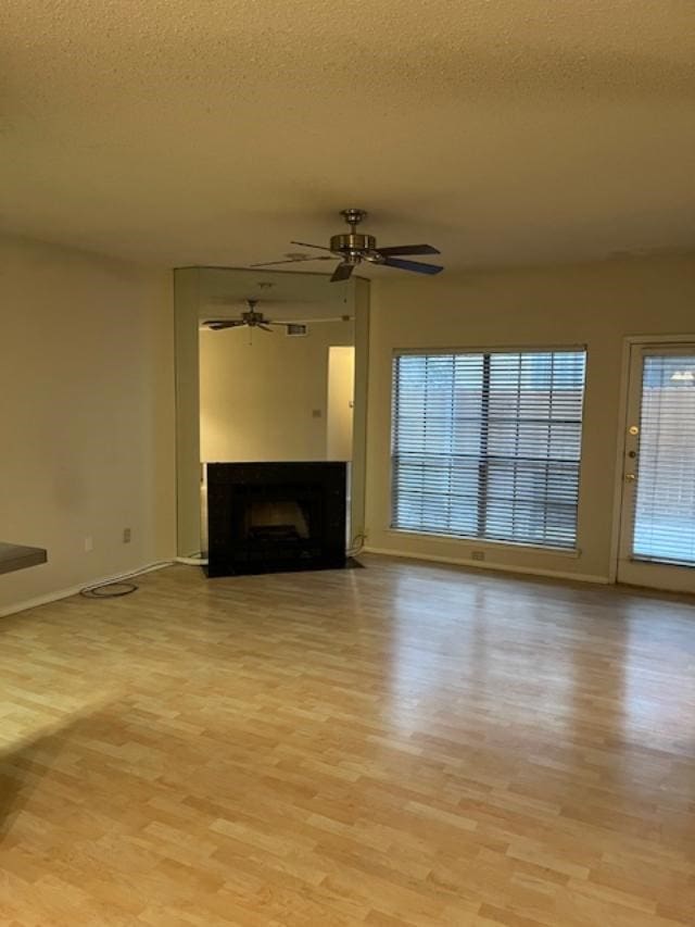 unfurnished living room with ceiling fan, a textured ceiling, and light wood-type flooring