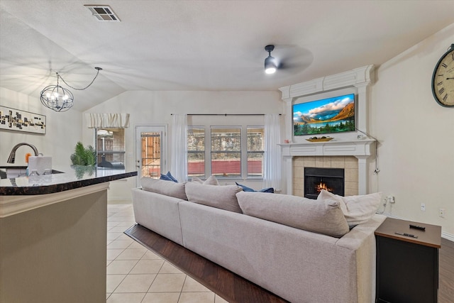 tiled living room with vaulted ceiling, a fireplace, and ceiling fan with notable chandelier