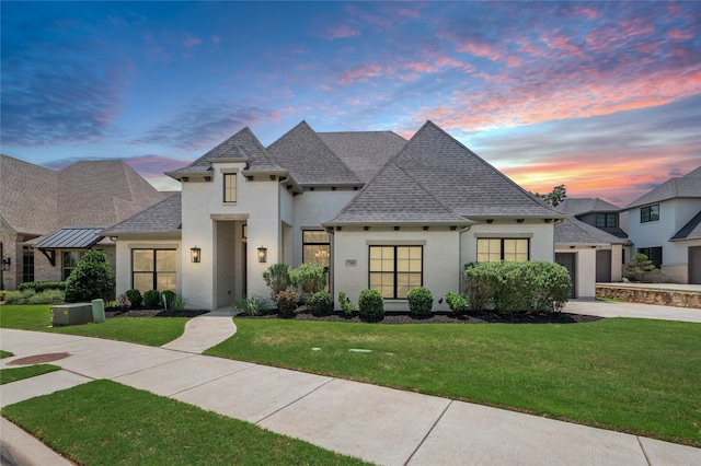 french country inspired facade with a garage, brick siding, a shingled roof, concrete driveway, and a front yard