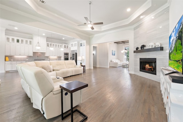 living room with a ceiling fan, a tile fireplace, ornamental molding, wood finished floors, and a tray ceiling