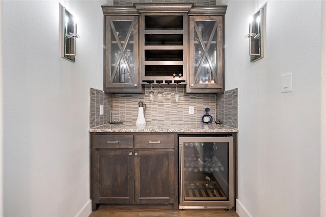 bar featuring dark wood finished floors, decorative backsplash, beverage cooler, bar, and baseboards